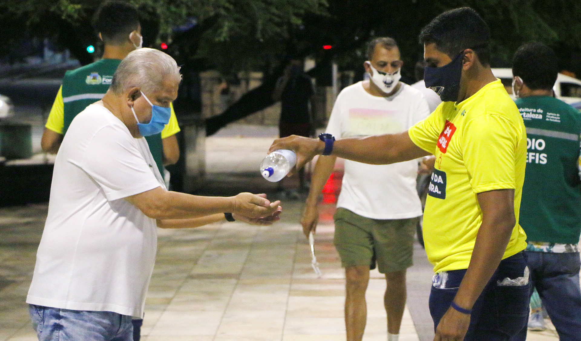 fiscal da agefis colocando álcool gel na mão de senhor que usa máscara